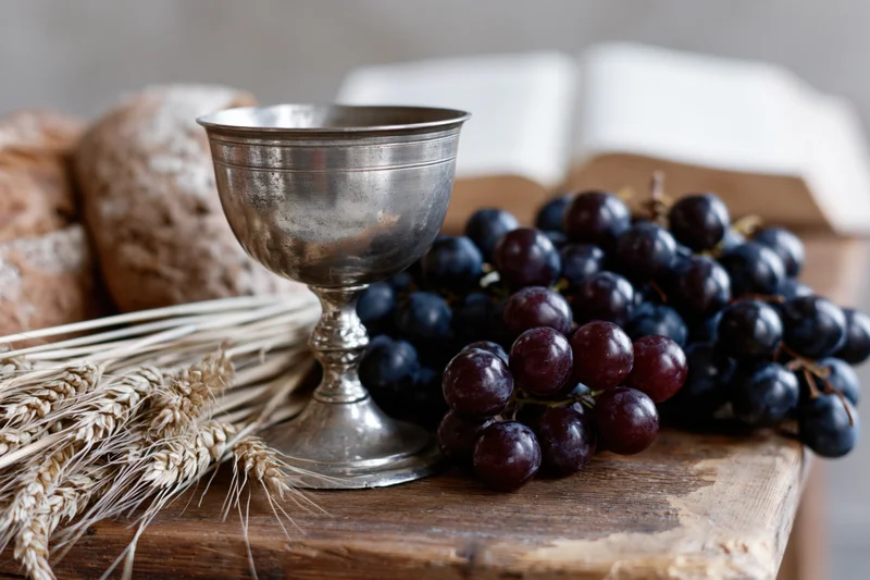 Pewter communion chalice with dark red grapes and wheat stalks on a rustic wooden table