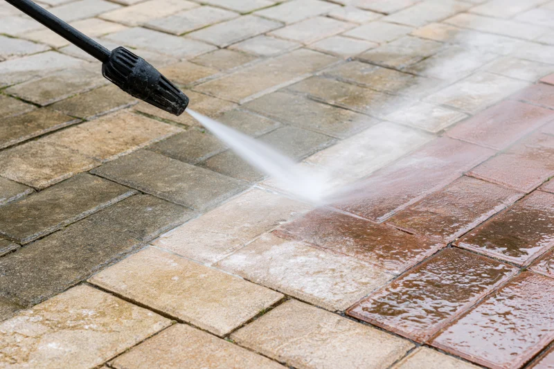 Pressure washer nozzle spraying water onto a brick paver patio surface