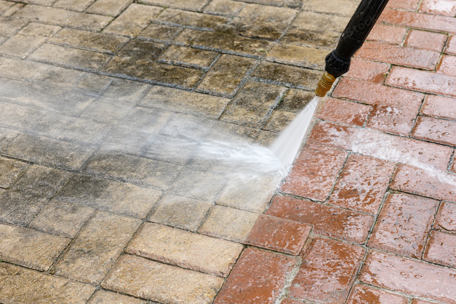 Pressure washer wand spraying water onto a brick paver patio surface