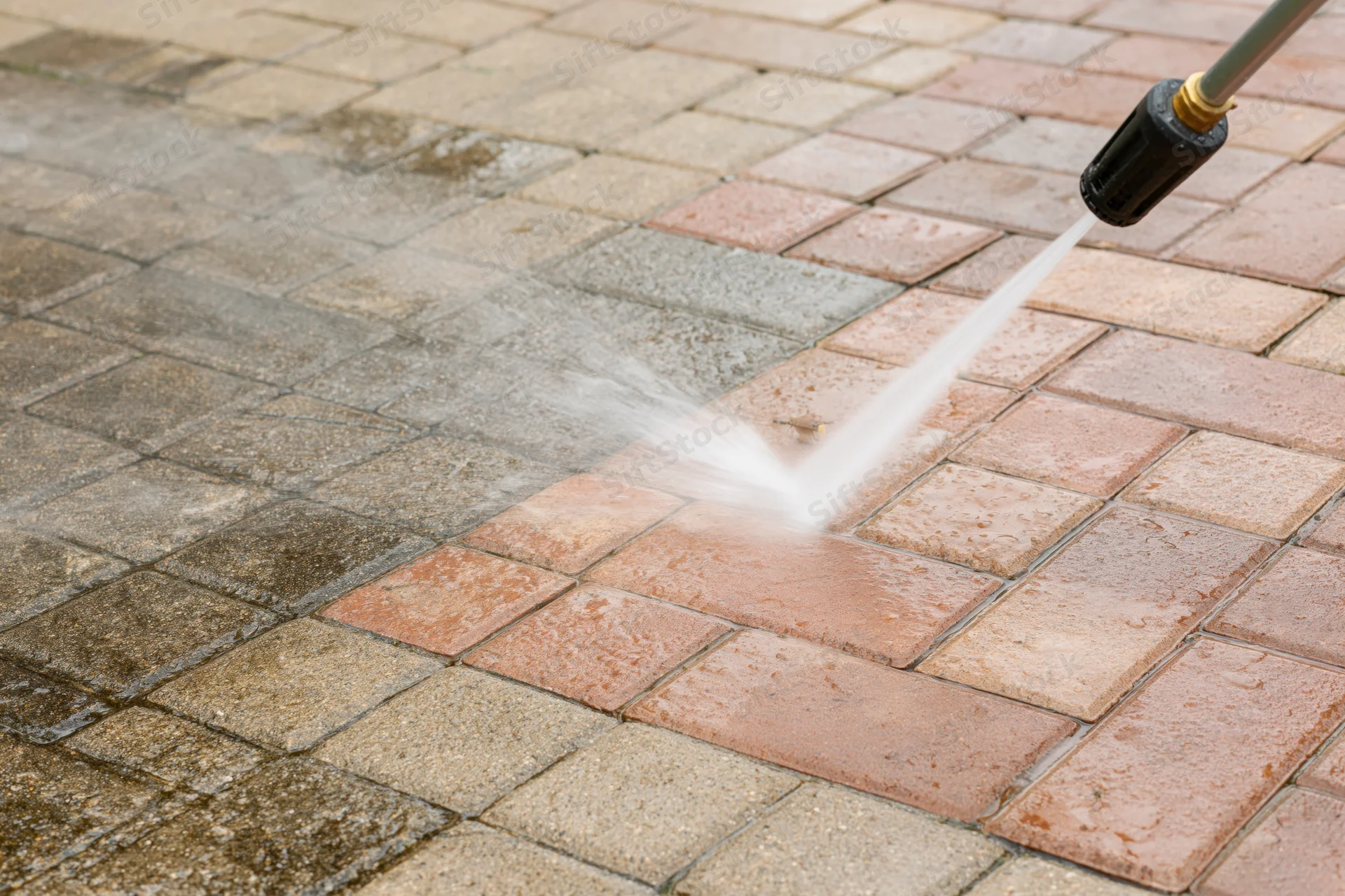 Pressure washer spraying water onto a brick paver patio surface