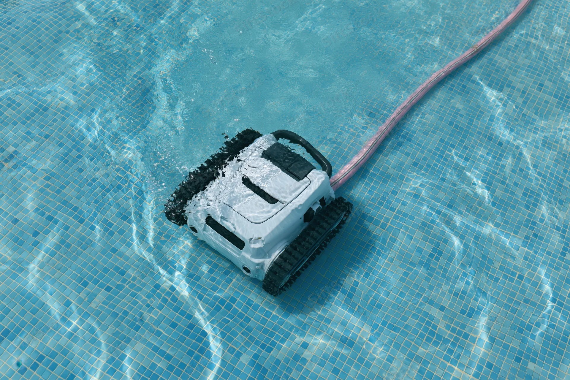 Robotic pool cleaner with black rubber tracks and white plastic body operating underwater in a tiled swimming pool