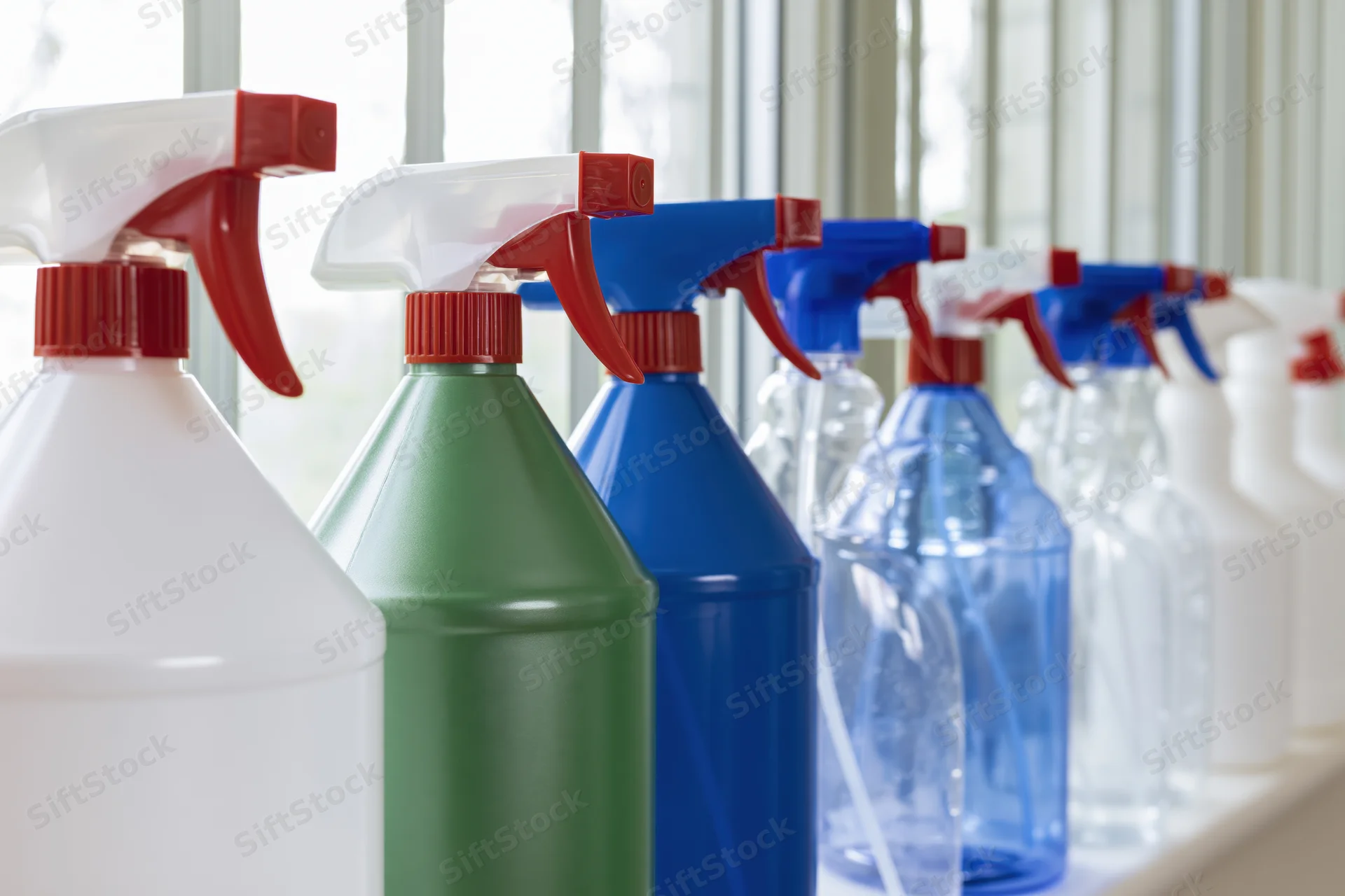 Row of household spray bottles with trigger nozzles lined up on a windowsill