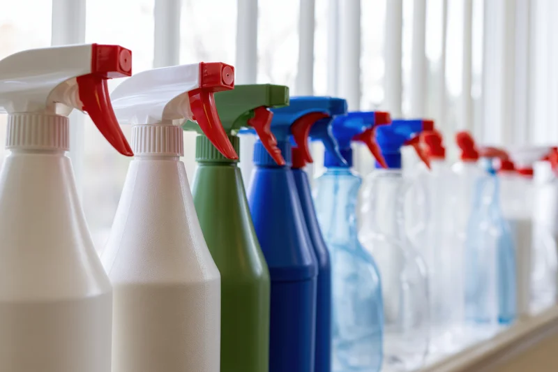 Row of household spray bottles with trigger nozzles lined up on a windowsill