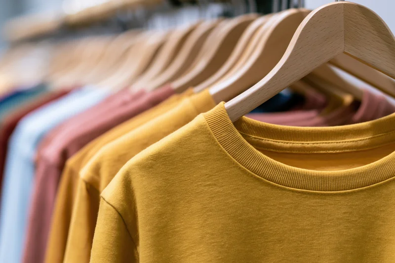 Row of plain cotton t-shirts hanging on wooden hangers in a retail display