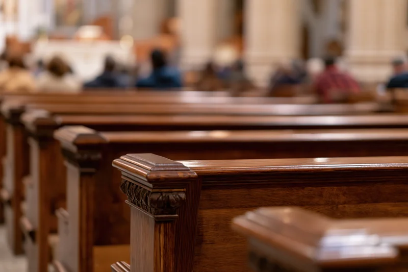 Rows of dark polished wooden church pews receding toward altar with congregation seated in background