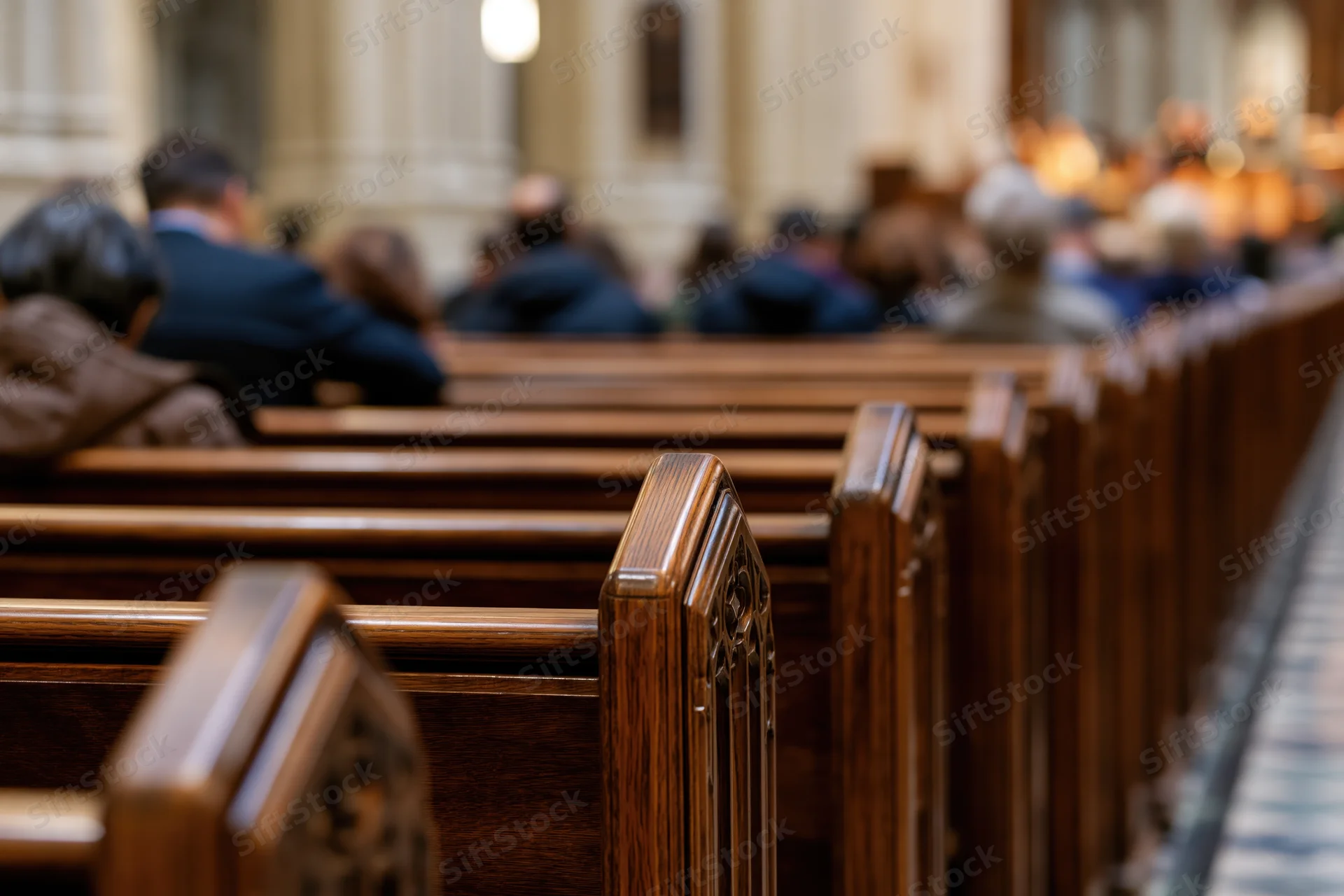 Rows of dark polished wooden church pews receding with congregation seated in background during service