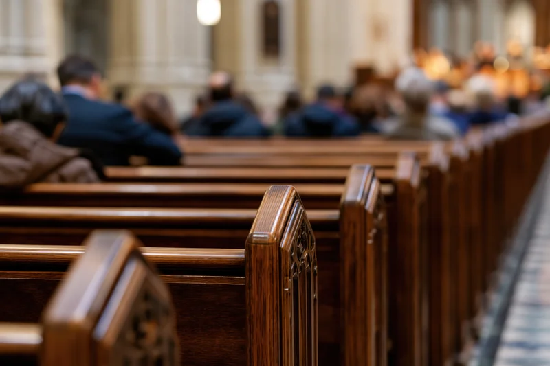 Rows of dark polished wooden church pews receding with congregation seated in background during service