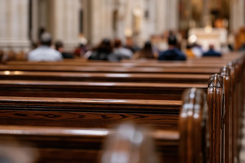 Rows of dark polished wooden pews receding in a church interior with blurred congregation in the background