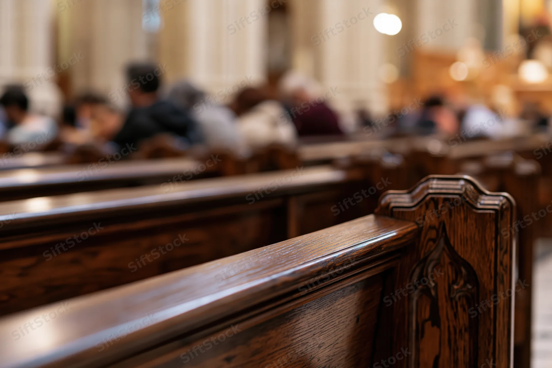 Rows of dark polished wooden church pews receding into the interior with people seated in the background