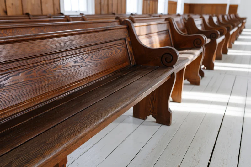 Rows of empty wooden church pews receding into the background along a white plank floor