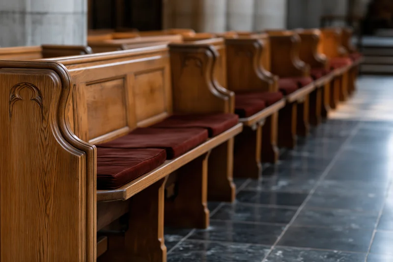 Rows of empty wooden church pews receding into the interior along a stone-tiled aisle