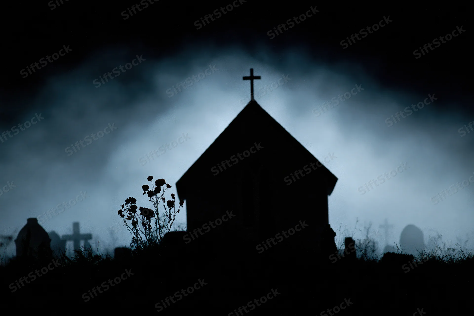 Silhouette of a gothic chapel with a cross on its peak in a foggy graveyard at night