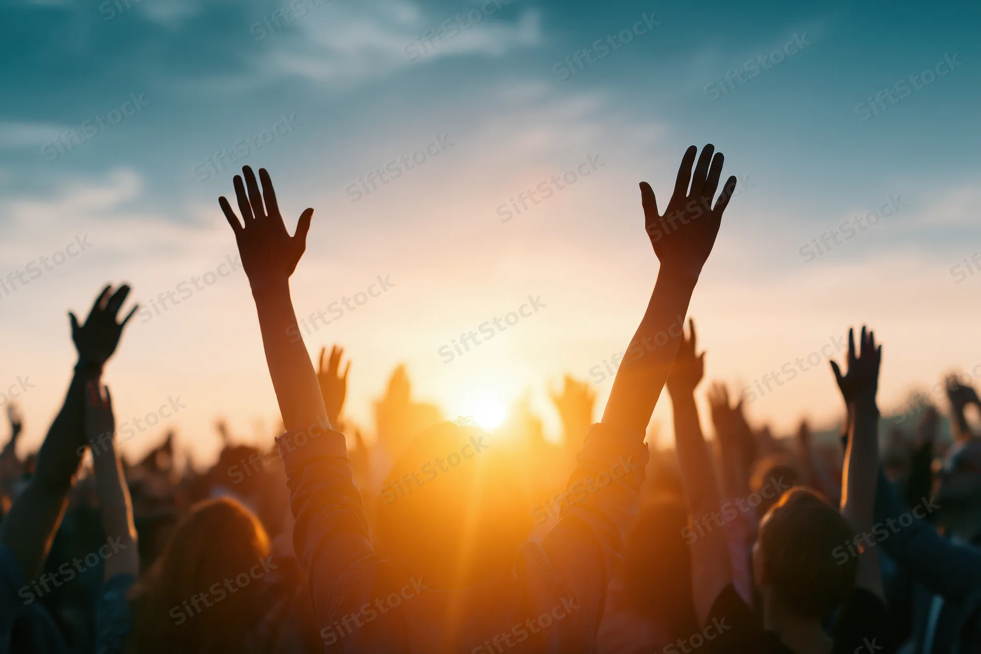 Silhouetted crowd raising hands toward sunset at outdoor concert
