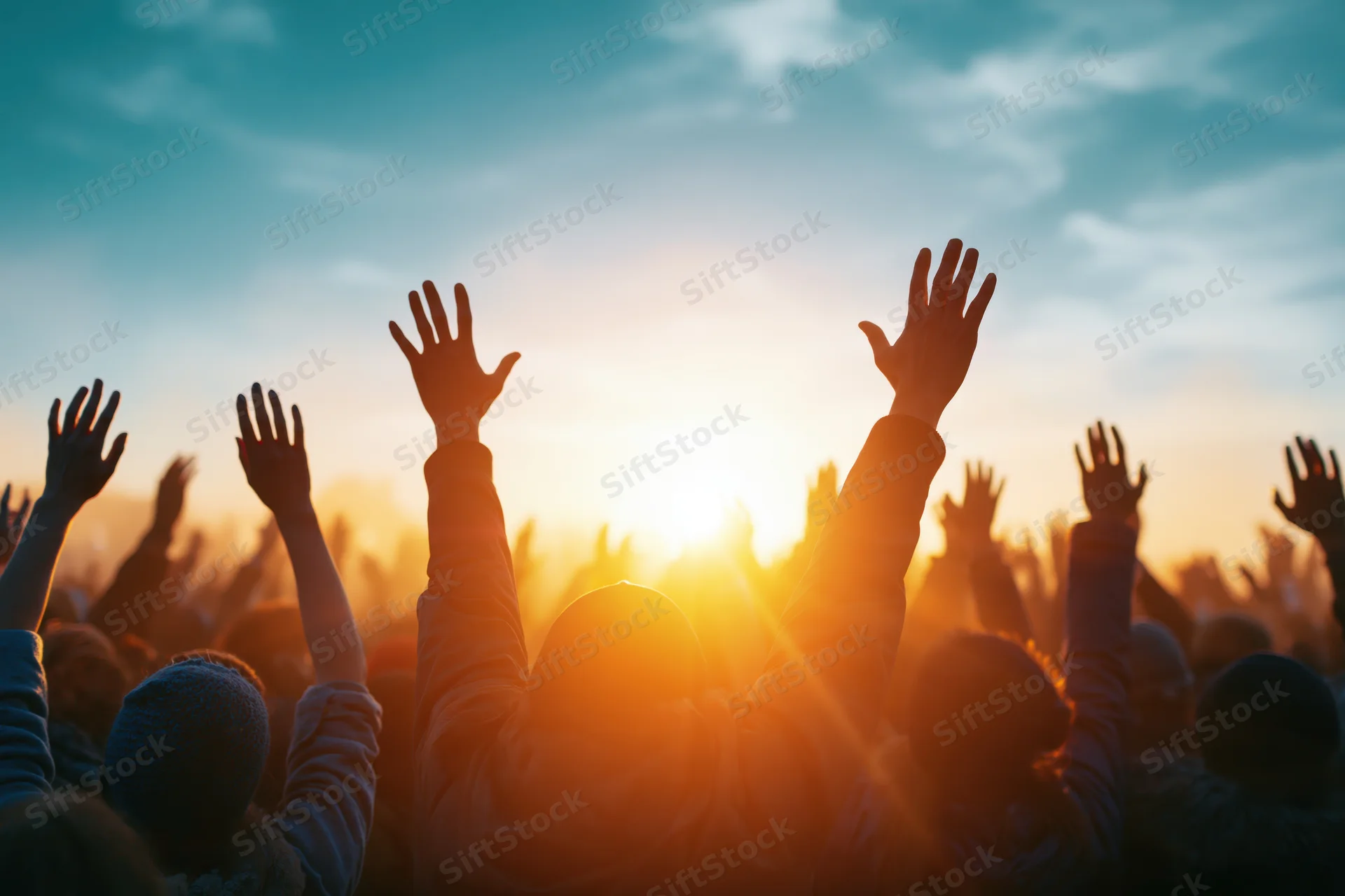 Silhouetted crowd raising hands toward sunset at outdoor event