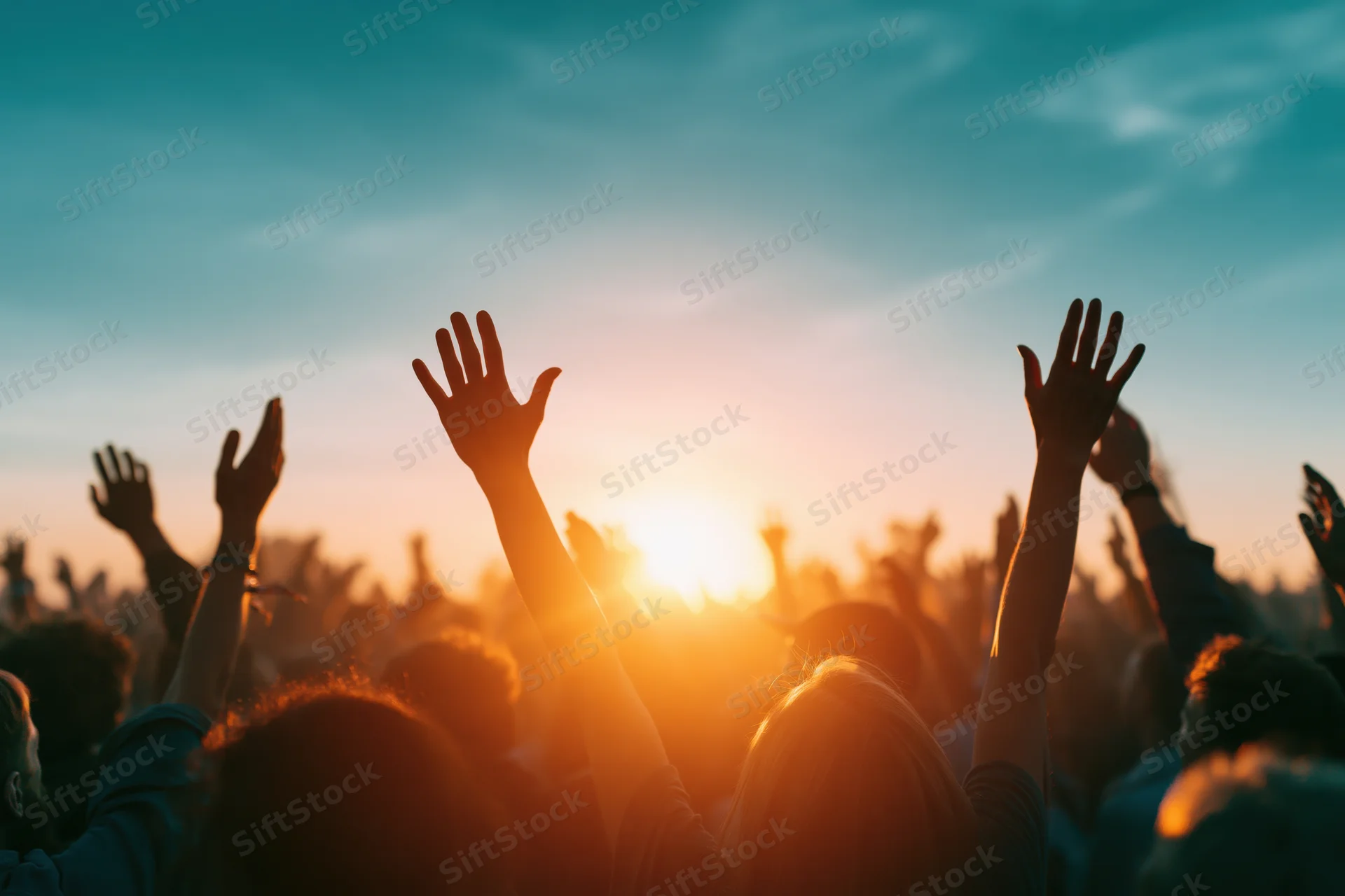 Silhouetted crowd raising hands toward sunset at outdoor music festival