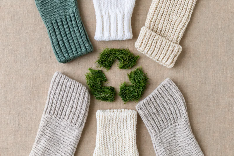 Six knitted socks arranged in a circle around a grass recycling symbol on a beige fabric background