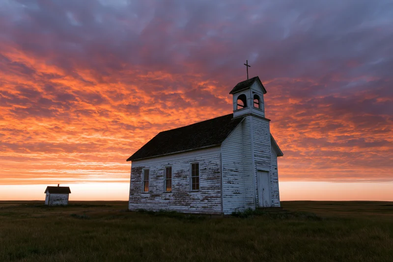 Small abandoned white clapboard church on prairie at sunset