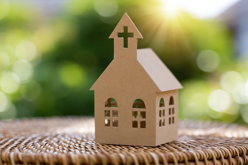 Cardboard church model standing on woven surface outdoors in sunlight