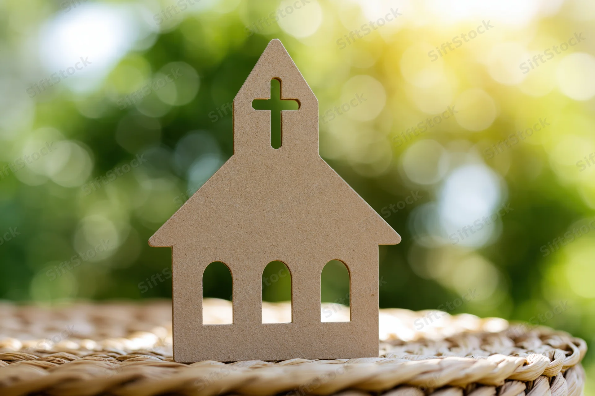 Cardboard church cutout standing on a woven wicker surface with green foliage and sunlight in the background