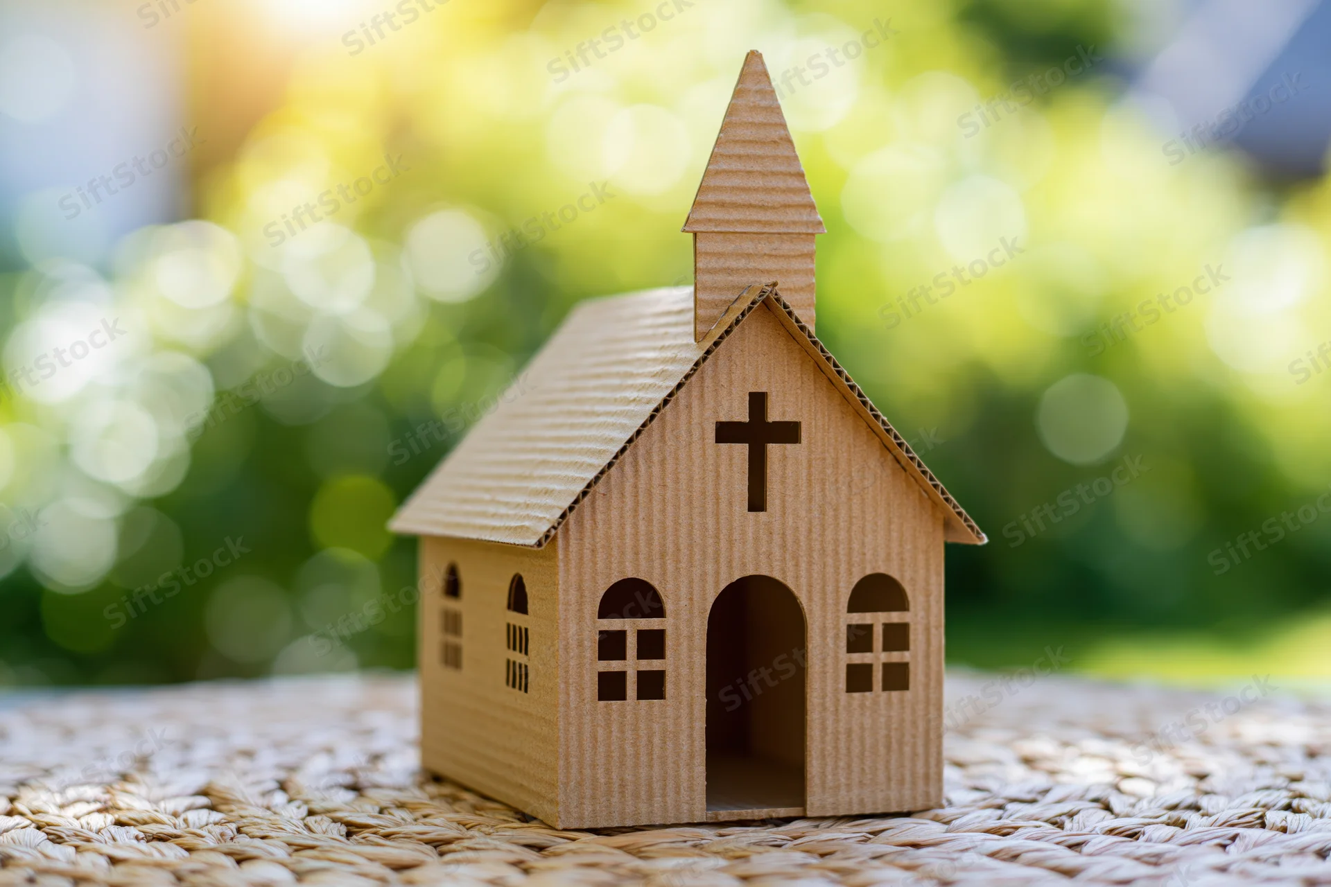 Small cardboard church model with cross on woven mat outdoors