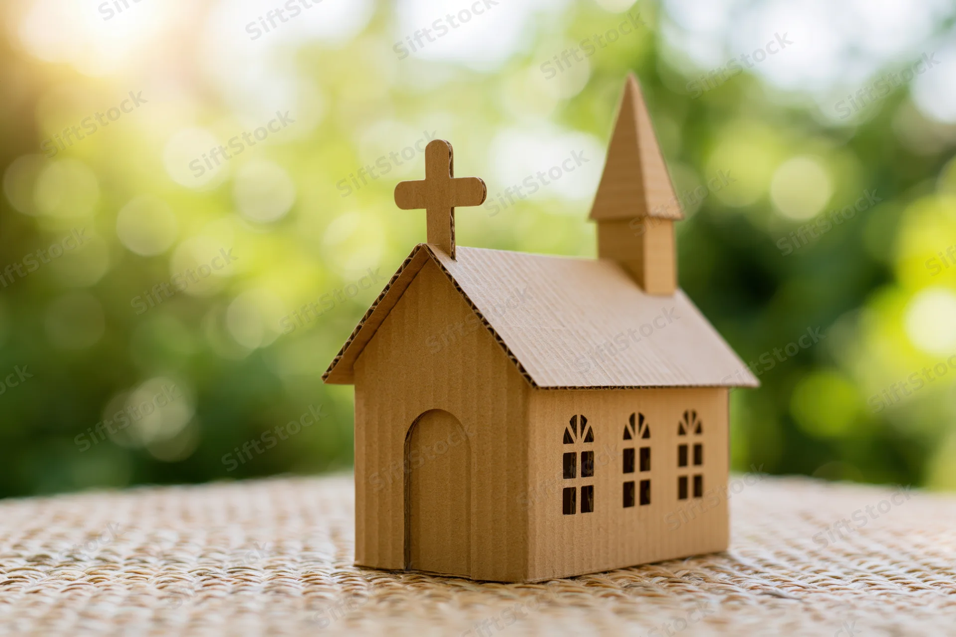 Small cardboard church model with cross on woven surface outdoors
