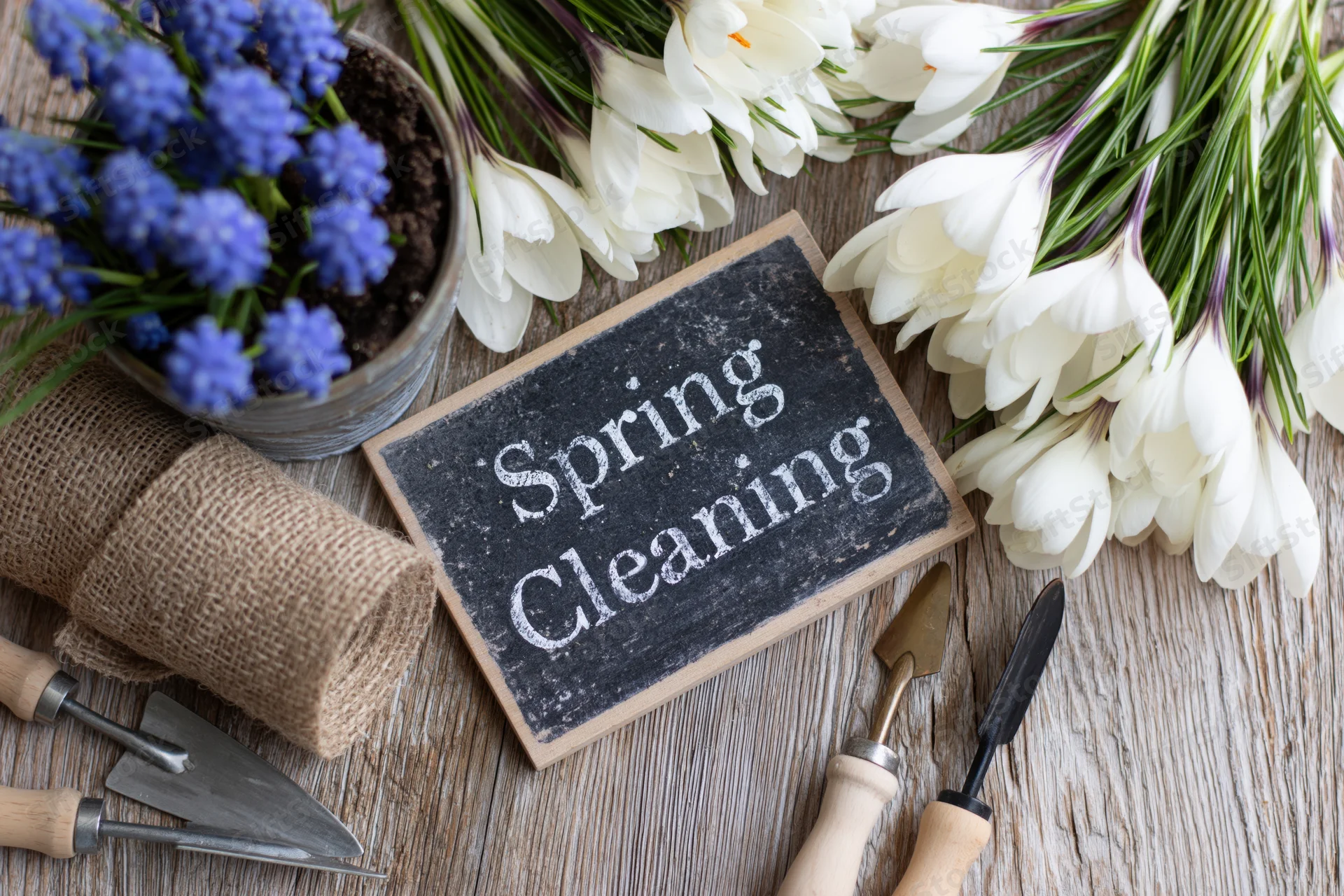 Chalkboard sign reading spring cleaning surrounded by crocus flowers and gardening tools on wooden surface