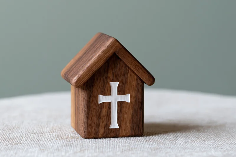 Small wooden church figurine with white cross on front, placed on textured fabric surface
