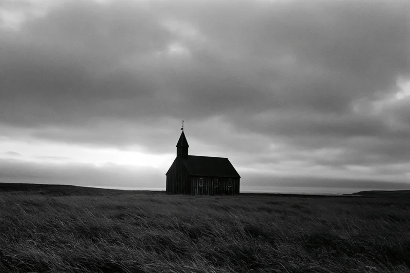 Small wooden church with steeple standing alone on grassy field under cloudy sky