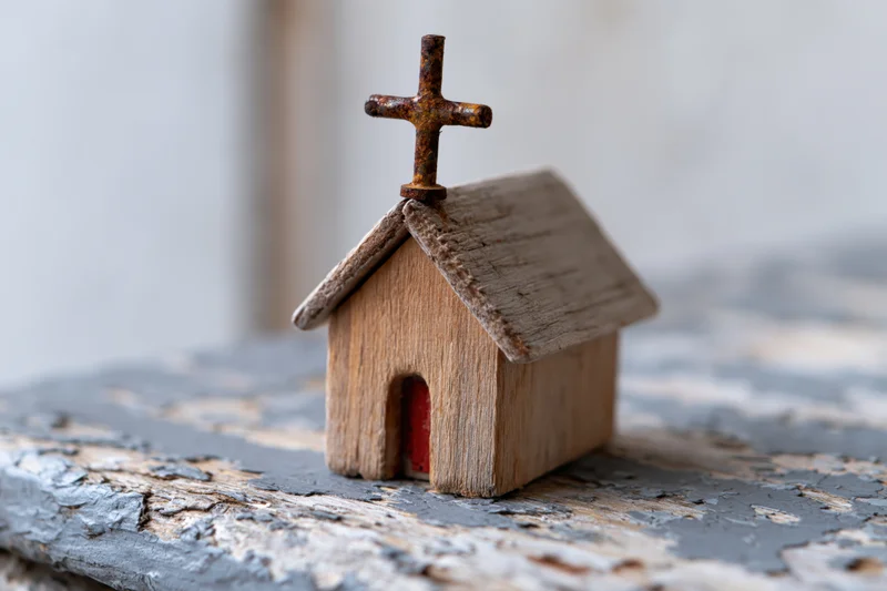 Small handmade wooden church figurine with rusty cross on weathered surface