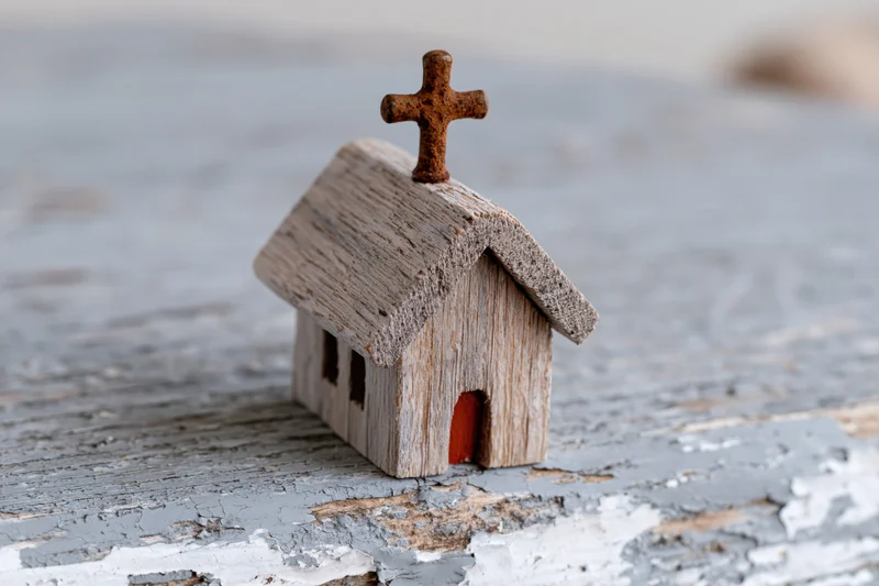 Small handmade wooden church figurine with rusty cross on weathered painted surface