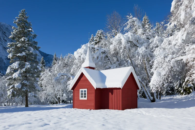 Small red wooden chapel with pointed steeple in snowy forested mountain landscape