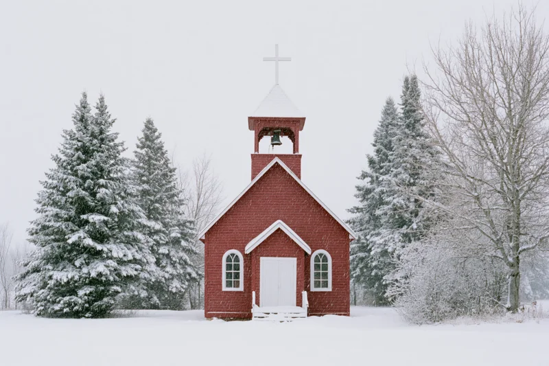 Small red wooden church with bell tower and white cross in snowy rural landscape