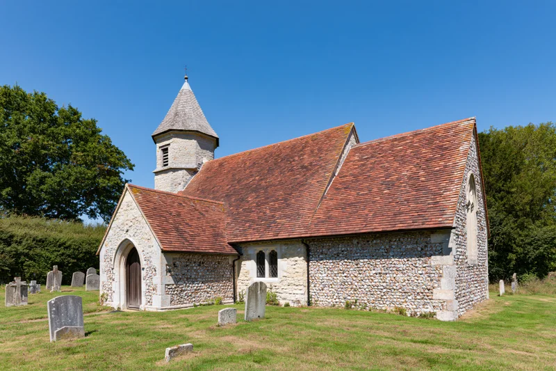 Small rural english parish church with stone walls and red tiled roof surrounded by graveyard on sunny day