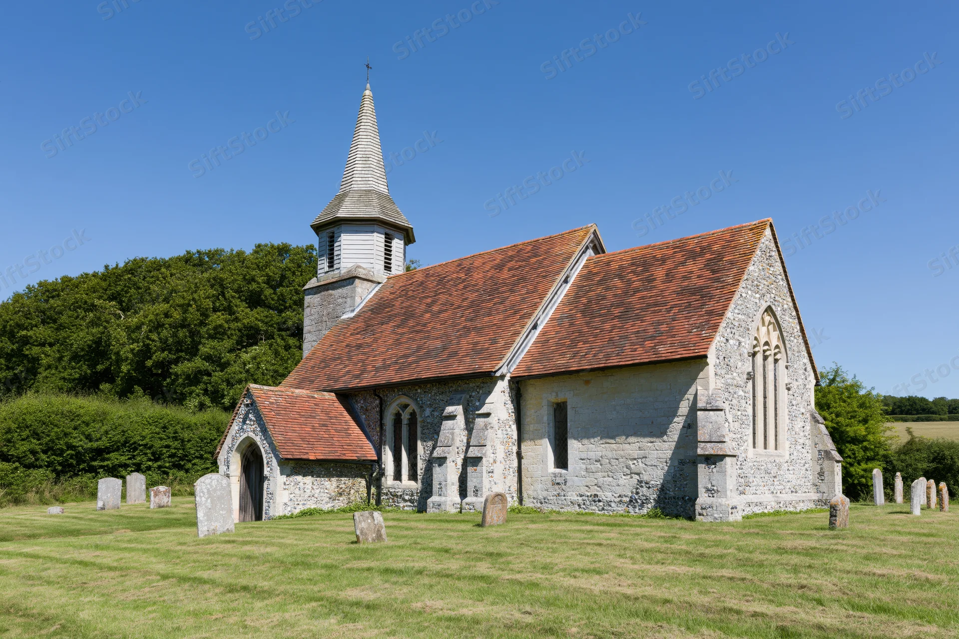 Small rural english parish church with stone walls and red tiled roof surrounded by graveyard on sunny day