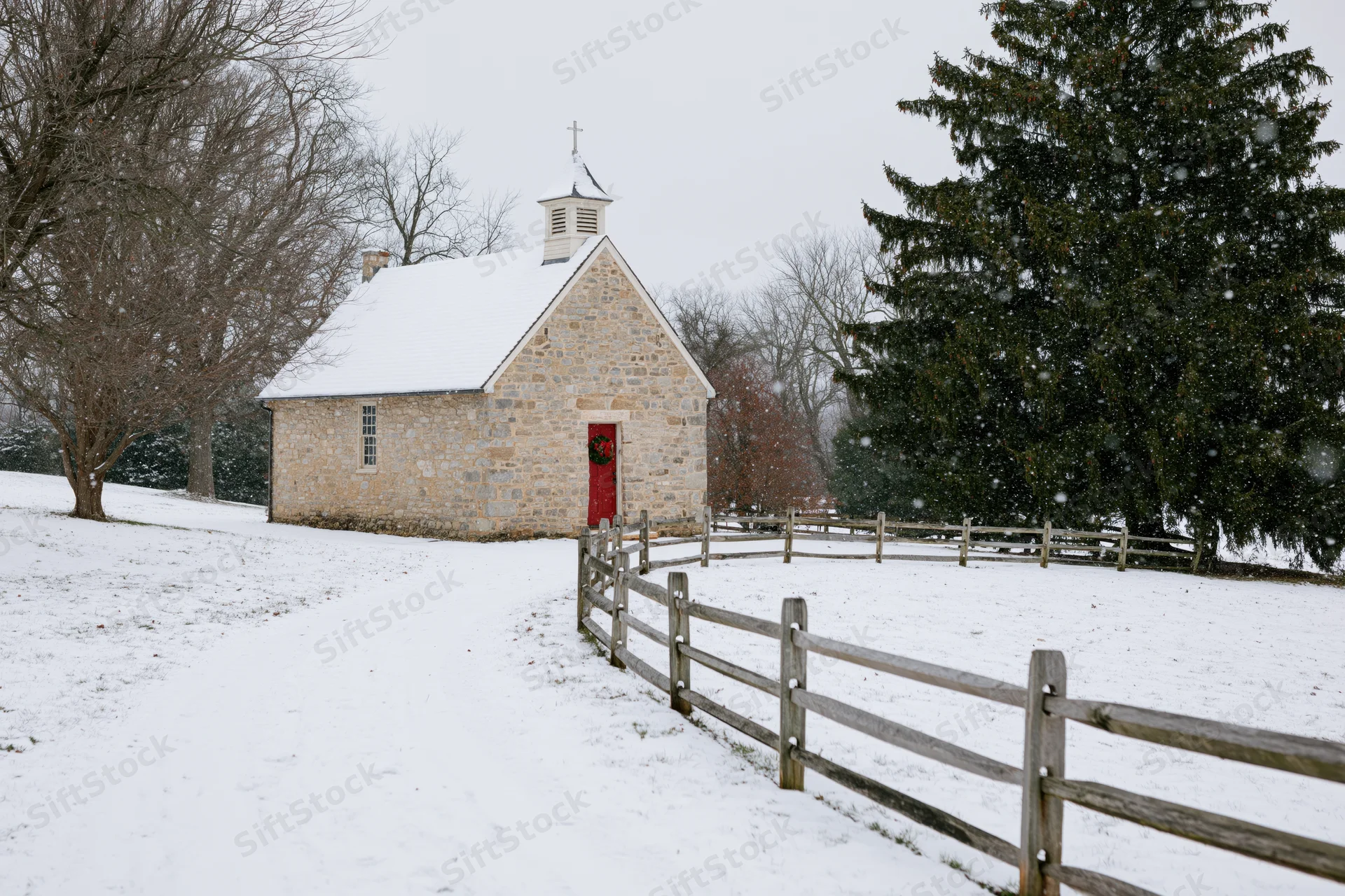 Small stone chapel with red door and christmas wreath in snowy rural landscape