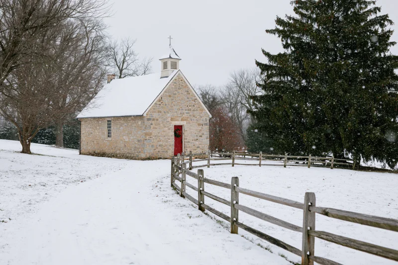 Small stone chapel with red door and christmas wreath in snowy rural landscape