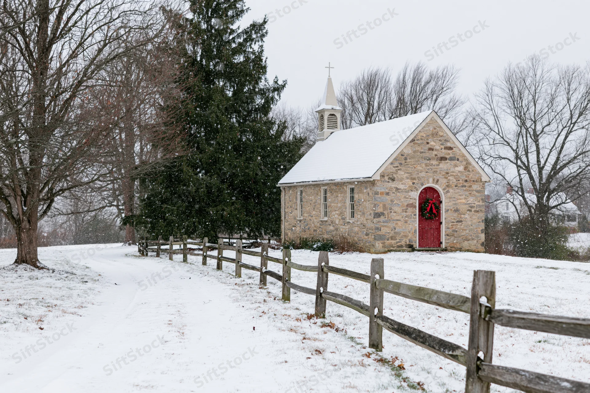 Small stone chapel with red door and christmas wreath in snowy rural landscape