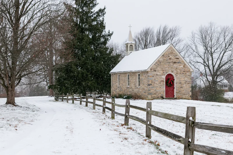 Small stone chapel with red door and christmas wreath in snowy rural landscape