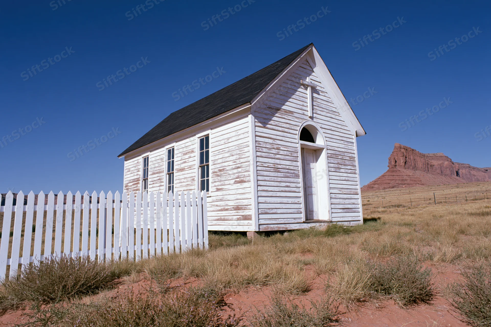 Weathered white wooden chapel with picket fence in desert landscape under blue sky