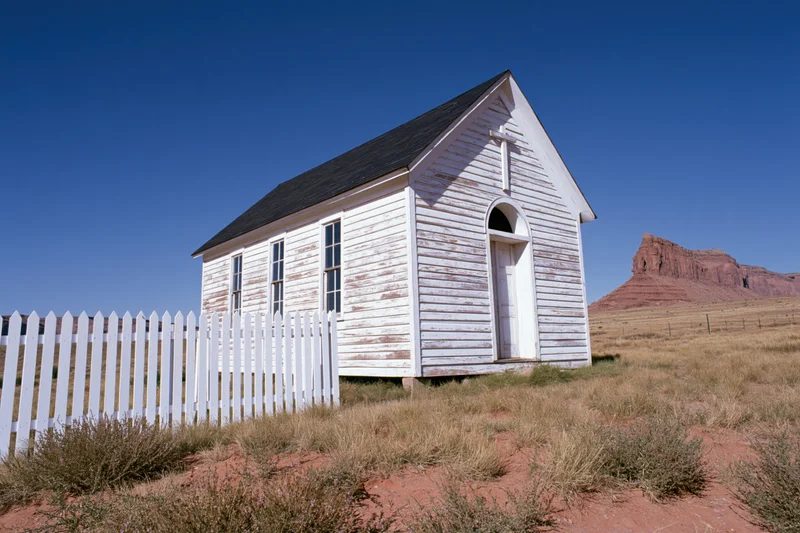 Weathered white wooden chapel with picket fence in desert landscape under blue sky