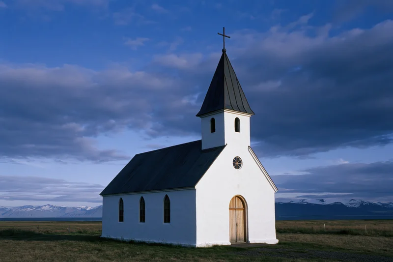 Small white church with dark metal steeple in rural icelandic countryside