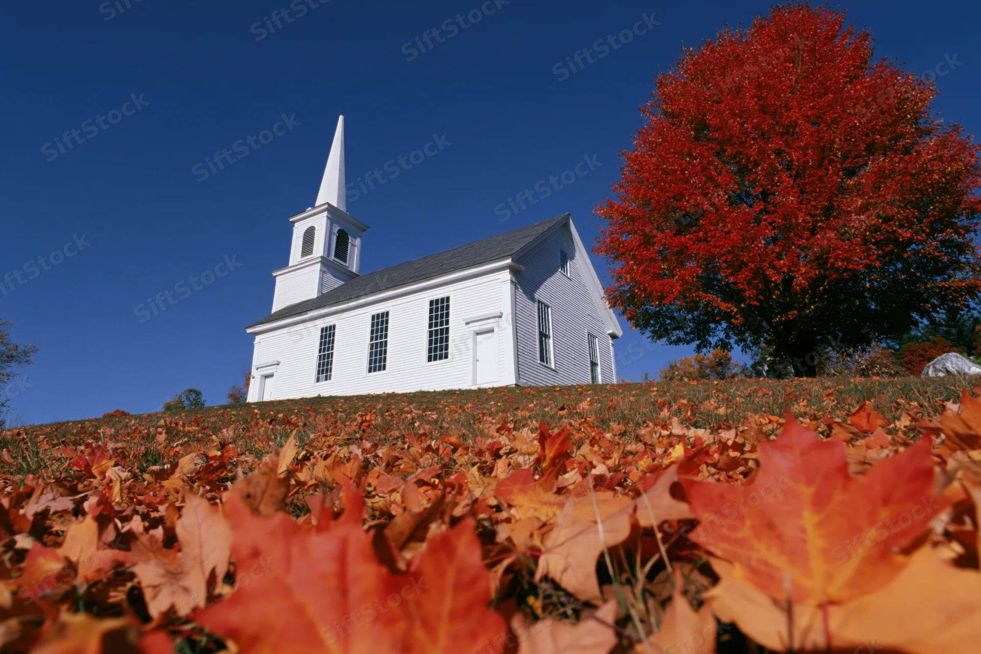 White clapboard church with steeple on a hill surrounded by autumn leaves under a clear blue sky