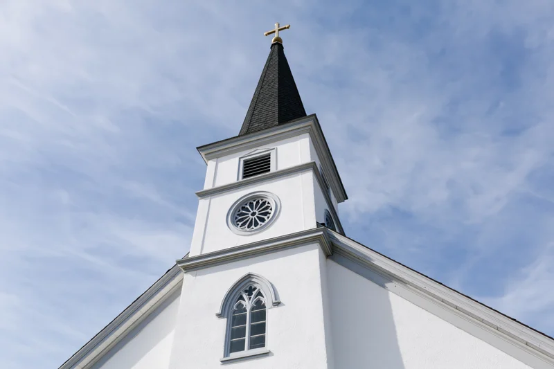 White protestant church facade with steeple and cross against blue sky