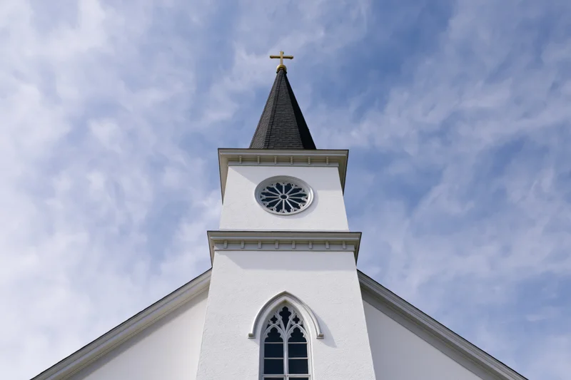 White protestant church facade with steeple and cross against blue sky