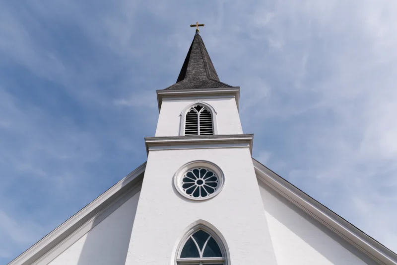 Low-angle view of white protestant church facade with steeple and cross against blue sky