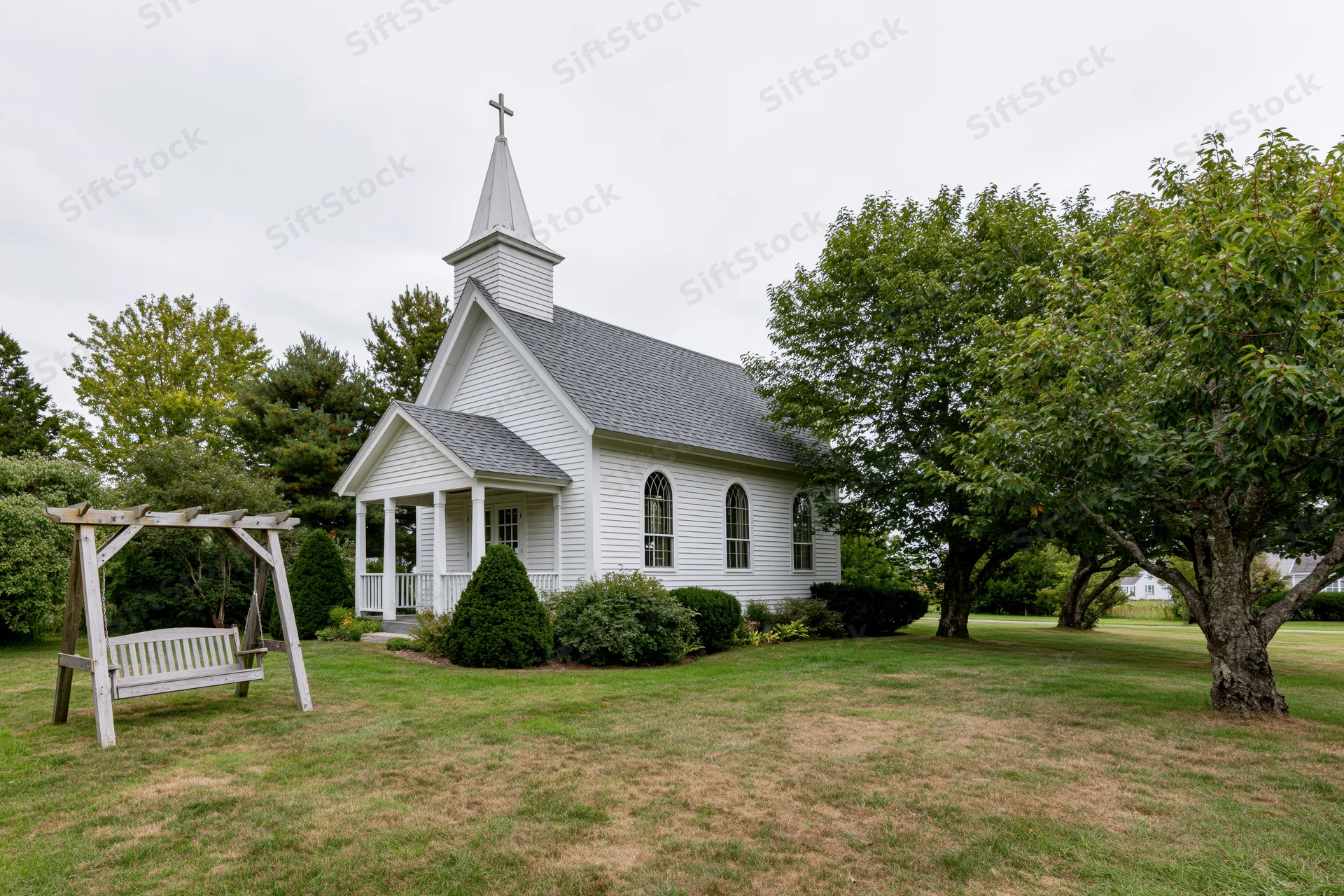 Small white clapboard chapel with cross-topped steeple and porch surrounded by green lawn and trees