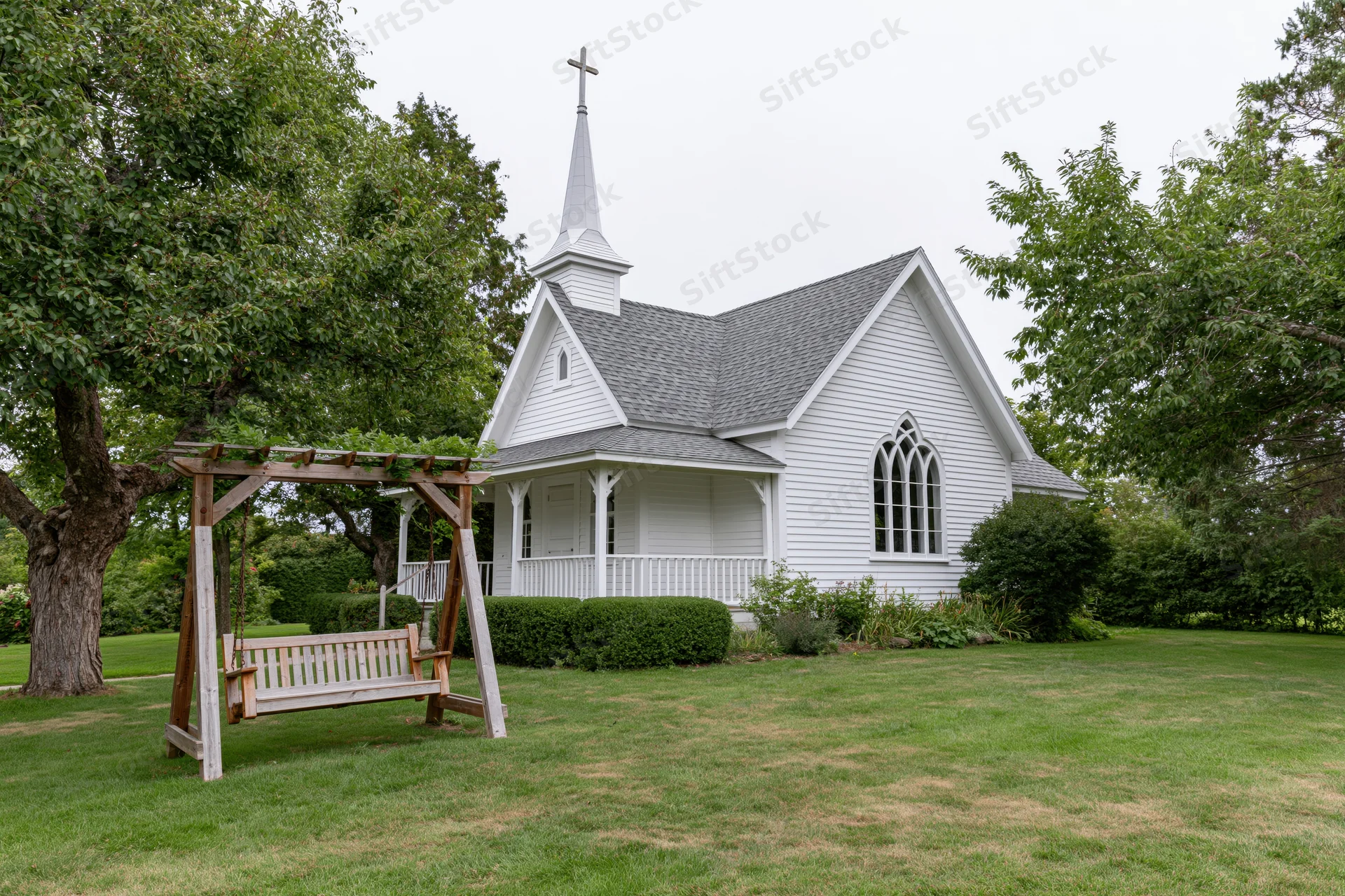 Small white clapboard chapel with cross-topped steeple and porch surrounded by green lawn and trees