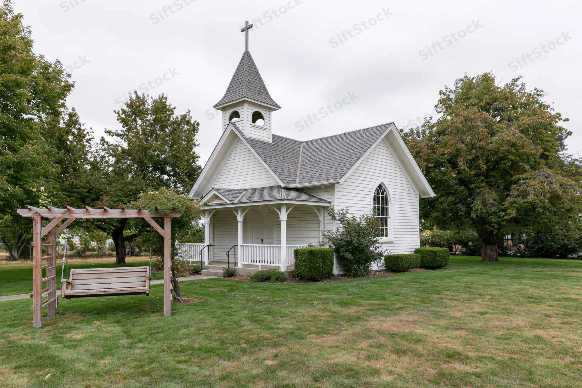 Small white clapboard chapel with cross-topped steeple and porch surrounded by green lawn and trees