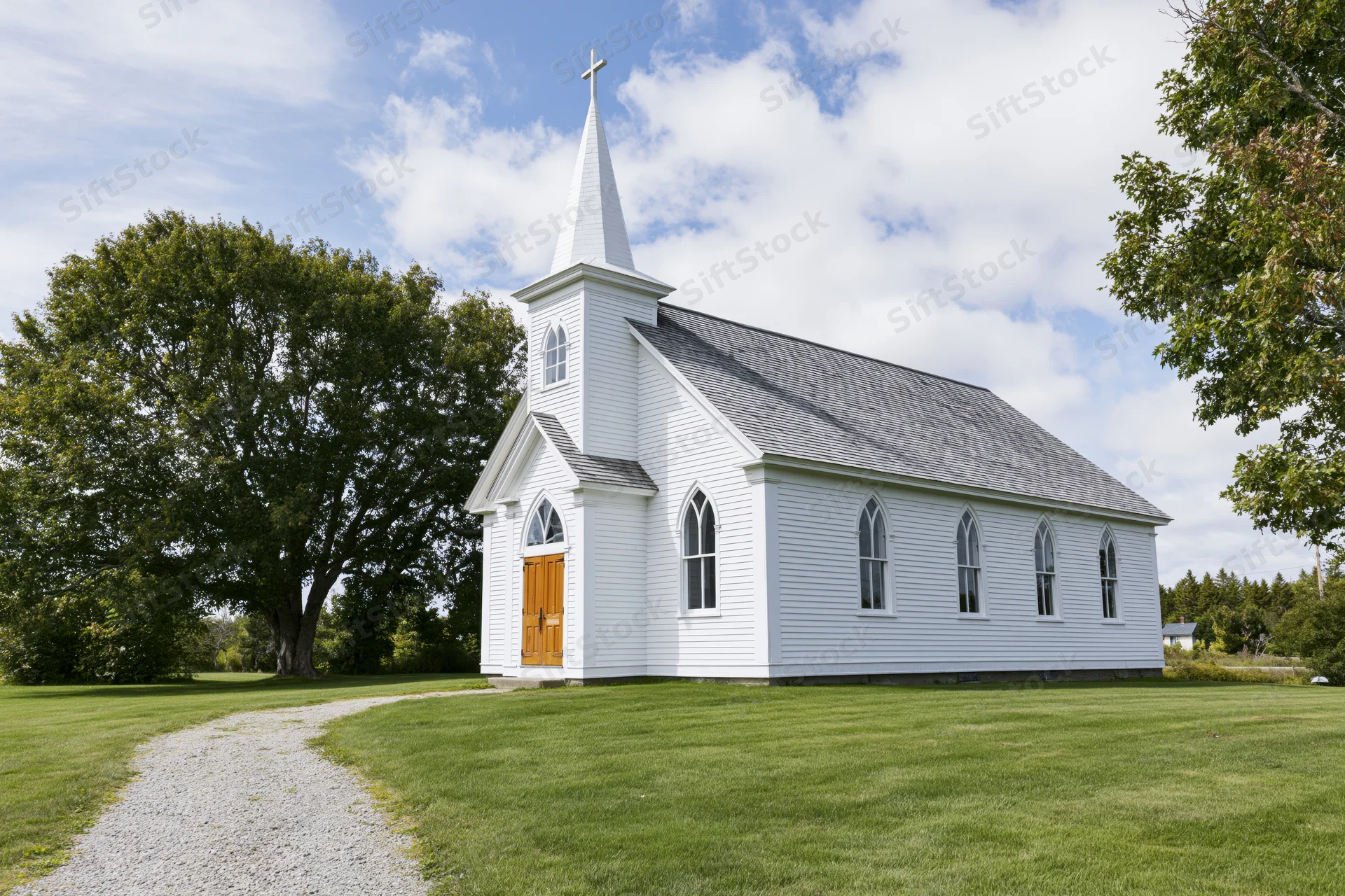 Small white clapboard country church with pointed steeple and arched windows on grassy lawn under blue sky