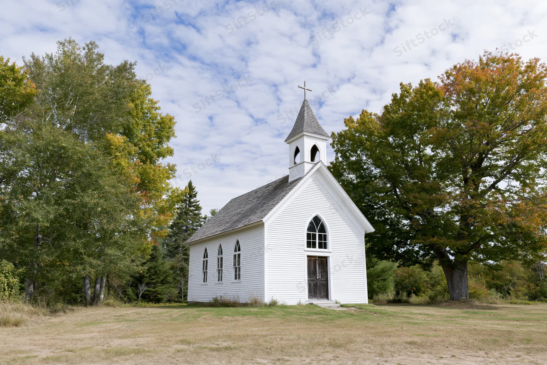 Small white clapboard church with steeple and cross in rural field surrounded by autumn trees